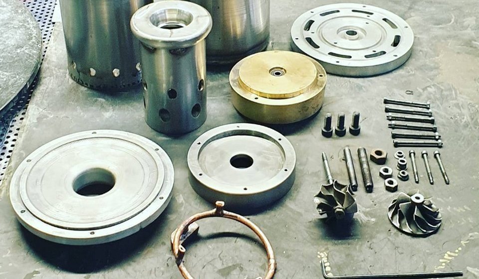Machined components of the micro gas turbine laid out on the workshop bench: casings, discs and fastener rings before assembly.